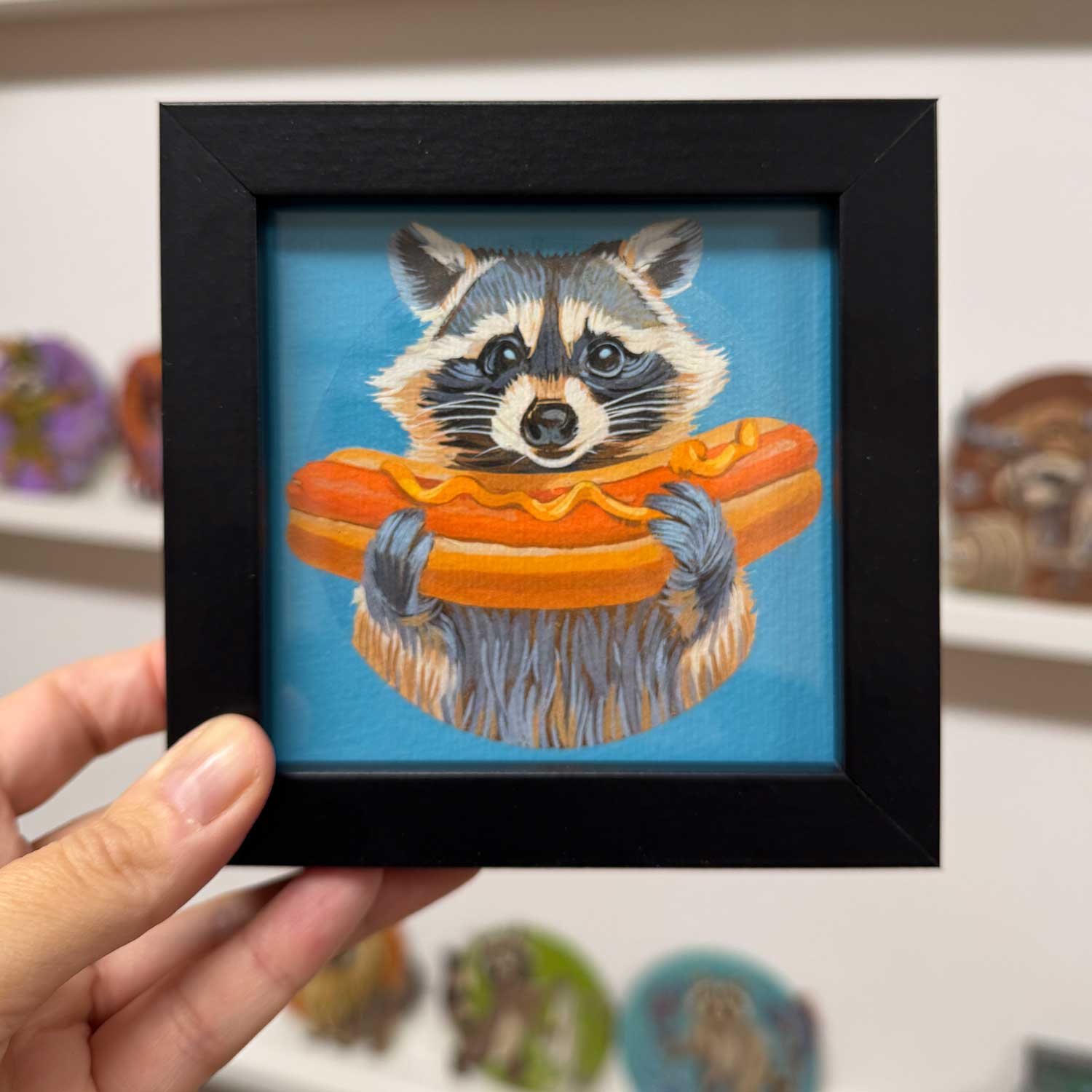 Cute raccoon holding a hot dog in a framed art print, perfect for adding charm to any space.