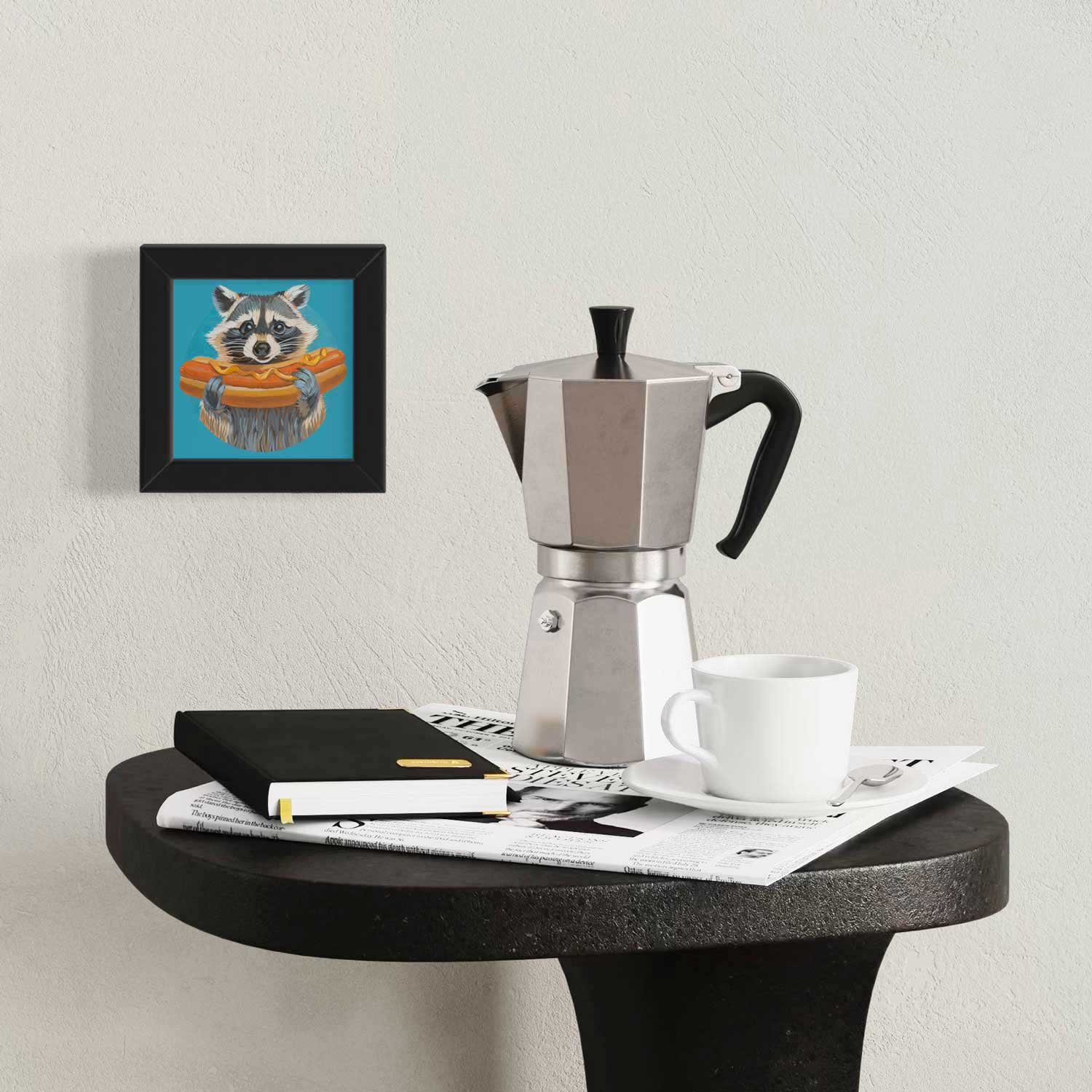 Cute raccoon art print beside a coffee maker on a stylish table, adding charm to any space.