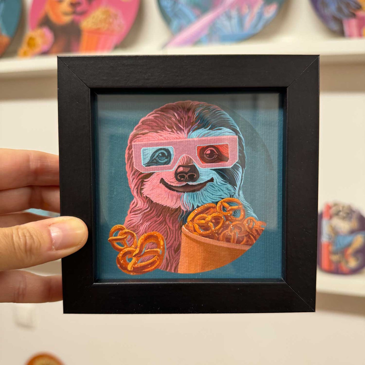 Cute sloth print in a black frame, enjoying pretzels and wearing 3D glasses, perfect for brightening up any space!