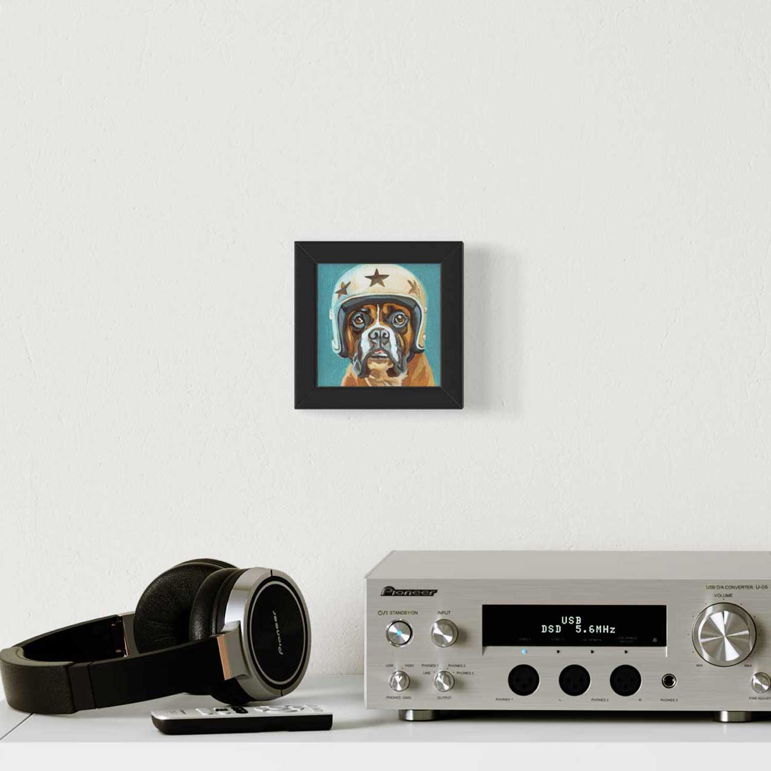 Cute framed art print of a dog in a helmet, adding charm to a modern living space with headphones and a sleek audio system.