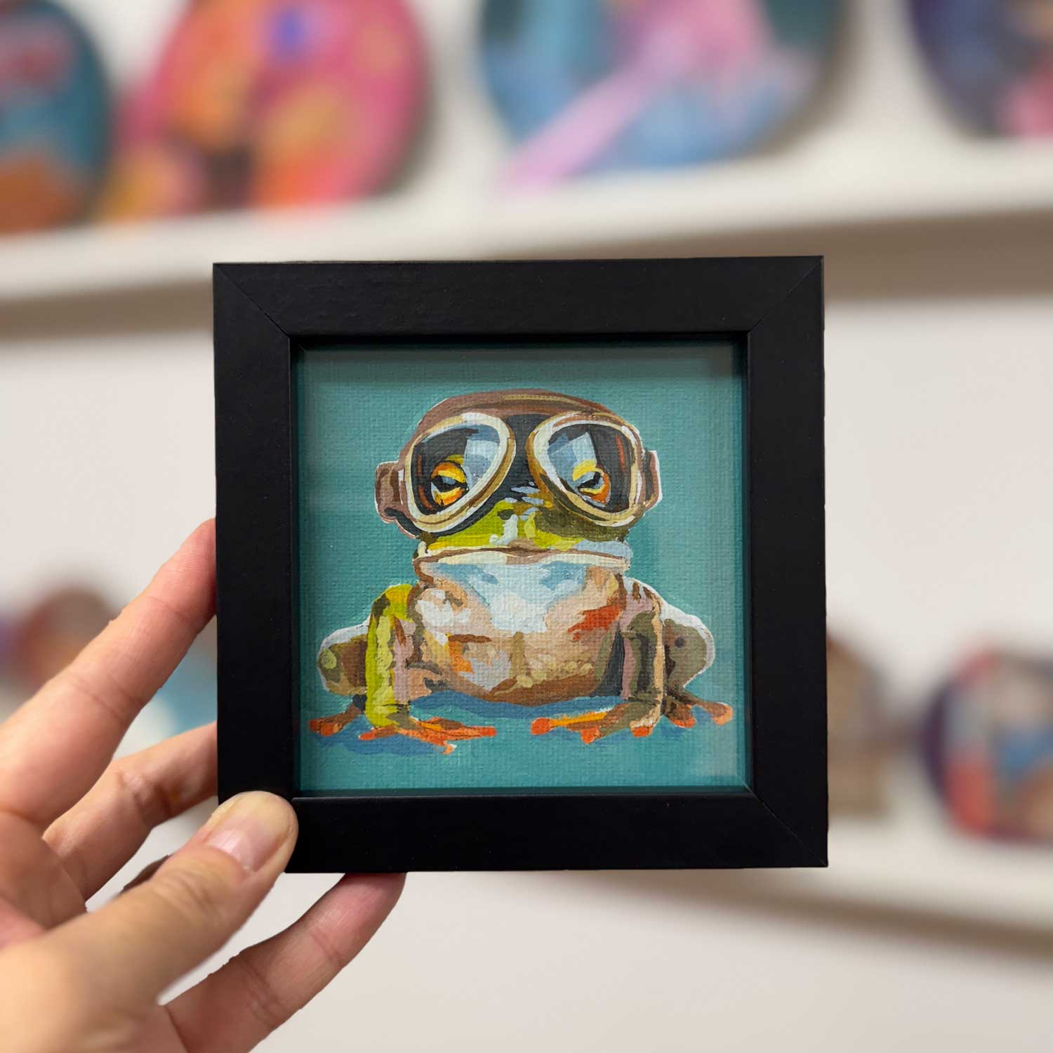 Cute framed art print of an adventurous frog in stylish glasses, perfect for home decor and adding a pop of color.