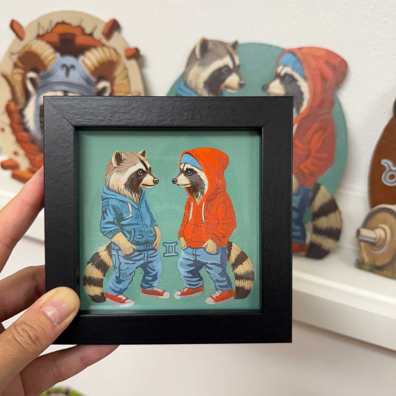 Cute framed art print of raccoons in hoodies representing the Gemini zodiac sign, perfect for home decor.