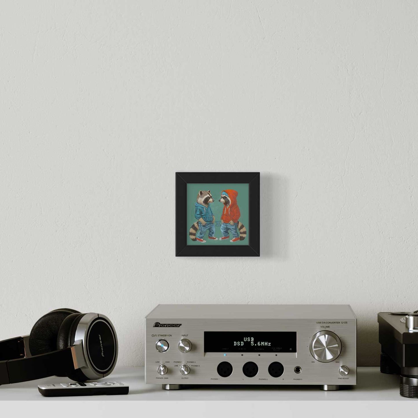 Cute raccoon art print in a black frame, adding charm to a modern living space above a stylish audio system.