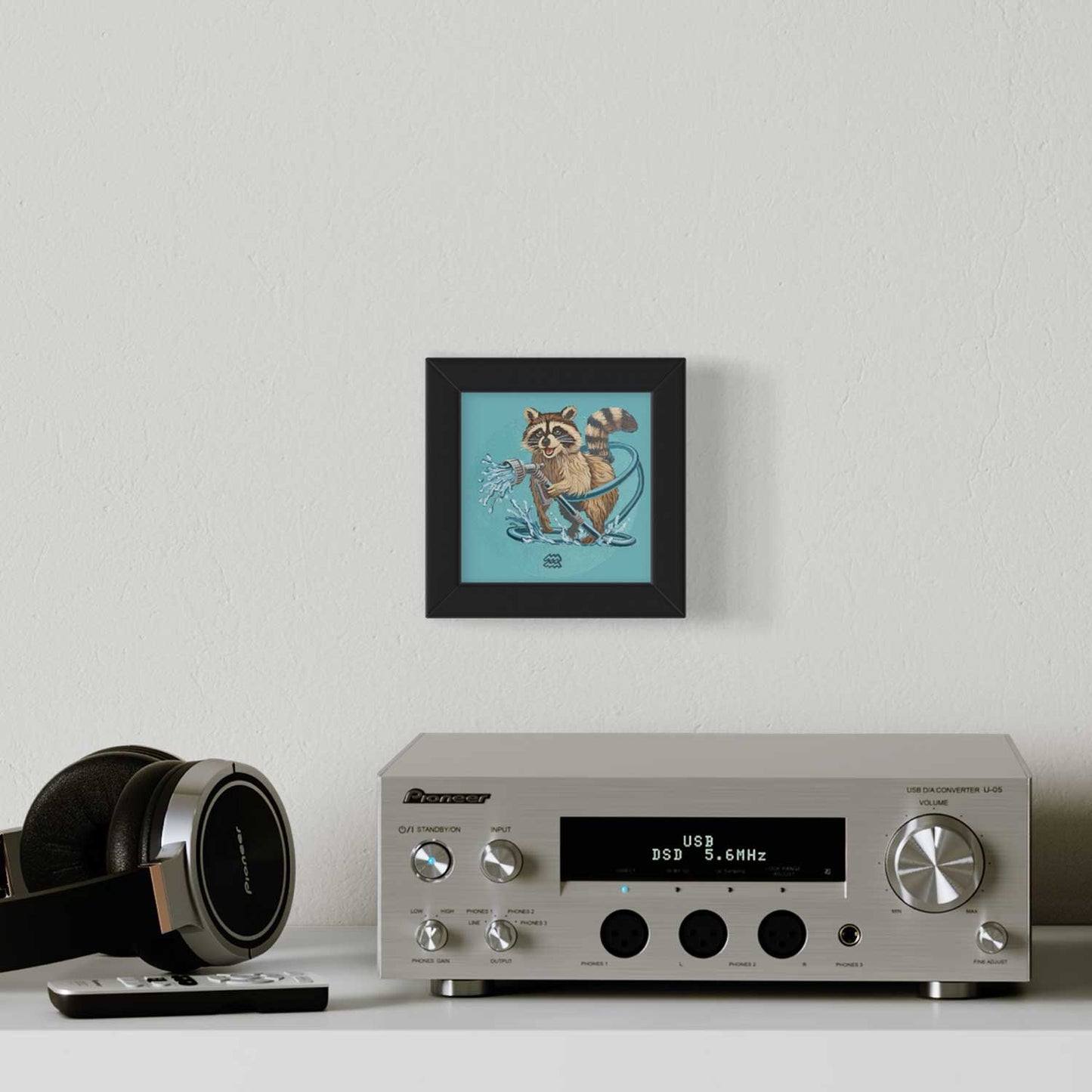 Cute raccoon art print in a black frame, brightening up a stylish room with a silver audio system.